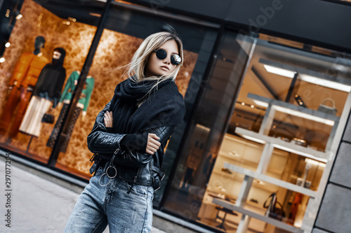 Stylish beauty woman in casual clothes walking on road on city street. Fashion outdoors portrait of trendy girl model on shops background