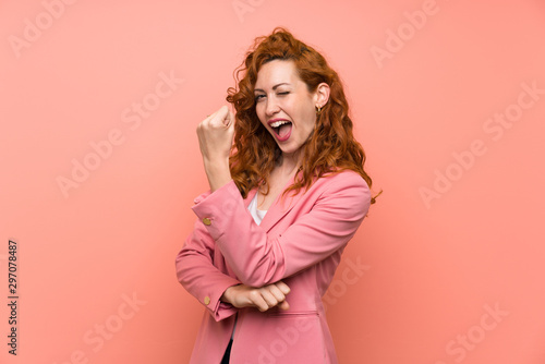 Redhead woman in suit over isolated pink wall making strong gesture