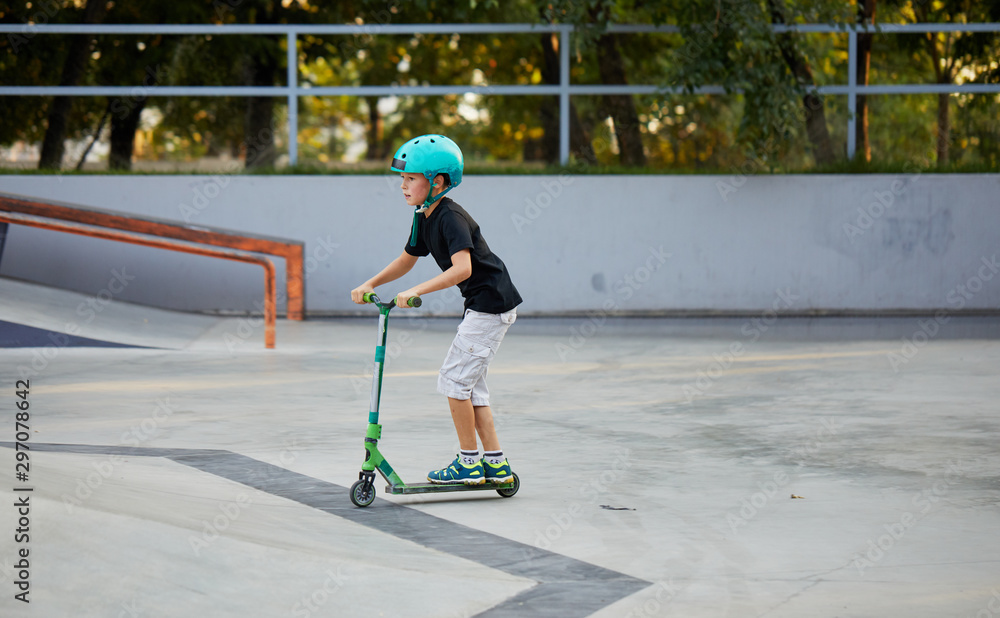 A boy on a scooter and in protective helmet do incredible stunts in skate park. Extreme jump. The concept of a healthy lifestyle and sports leisure A boy on a scooter and in protective helmet do incredible stunts in skate park. Extreme jump. The concept of a healthy lifestyle and sports leisure