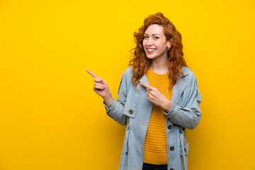 Redhead woman over isolated yellow background pointing finger to the side
