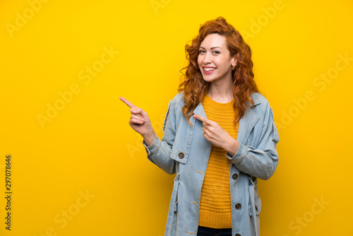 Redhead woman over isolated yellow background pointing finger to the side