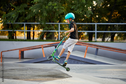 A boy on a scooter and in protective helmet do incredible stunts in skate park. Extreme jump. The concept of a healthy lifestyle and sports leisure