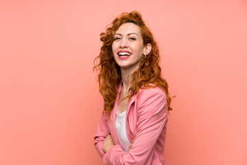 Redhead woman in suit over isolated pink wall laughing