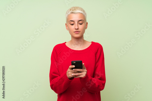 Teenager girl with white short hair over green wall sending a message with the mobile