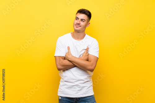 Young handsome man over isolated yellow background looking up while smiling