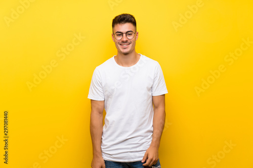 Young handsome man over isolated yellow background with glasses and happy