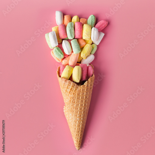 Ice cream cone with colored candies on pink pastel background. Flat lay.  photo