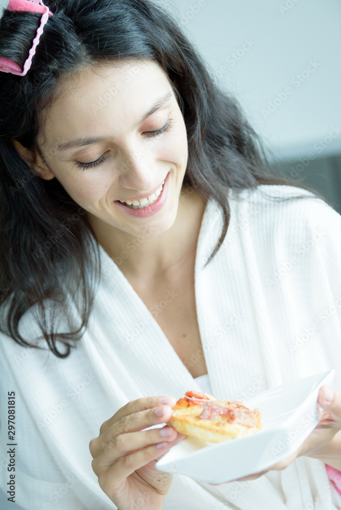 A beautiful woman wearing a towel and a white bathrobe has to eat a pizza with happy and relaxing on the bed at a condominium in the morning. A beautiful woman wearing a towel and a white bathrobe has to eat a pizza with happy and relaxing on the bed at a condominium in the morning.