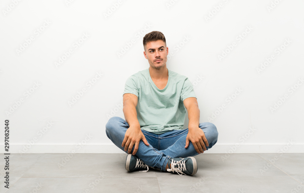 Young handsome man sitting on the floor standing and looking to the side