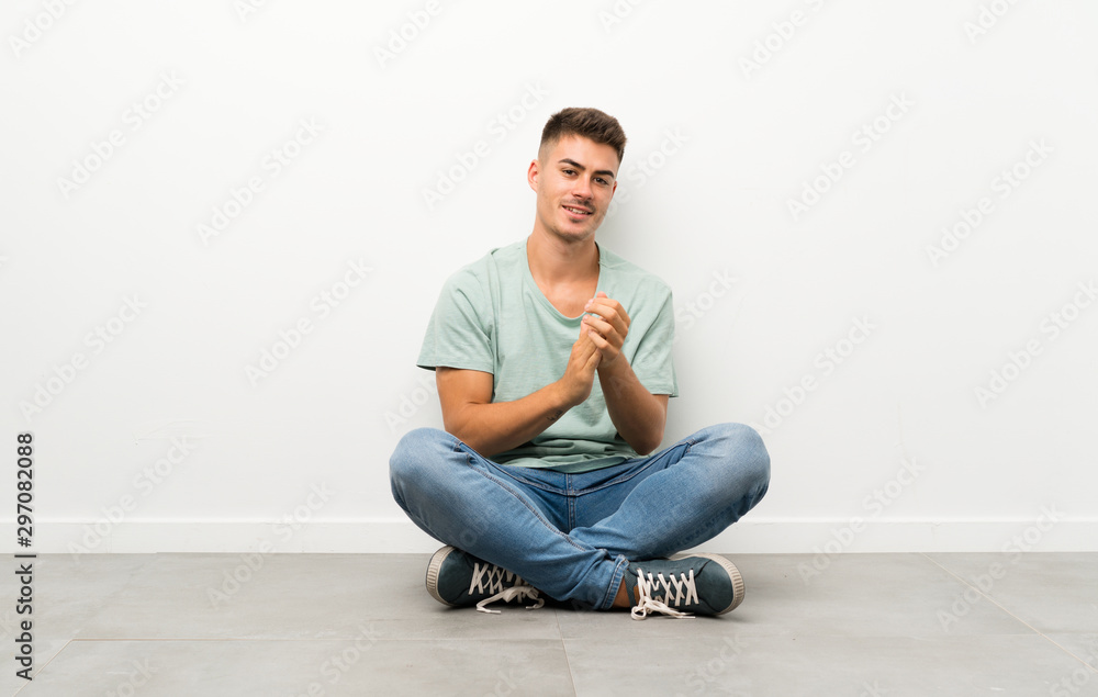 Young handsome man sitting on the floor applauding