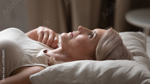 Valokuva Disturbed mature older woman lying awake in uncomfortable bed