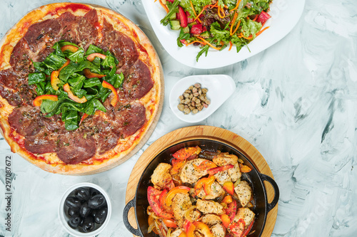 Table with planty of food for lunch, healthy salad, pizza with vitello tonatto veal and Meat chicken pan with tomatoes. Flat lay food table