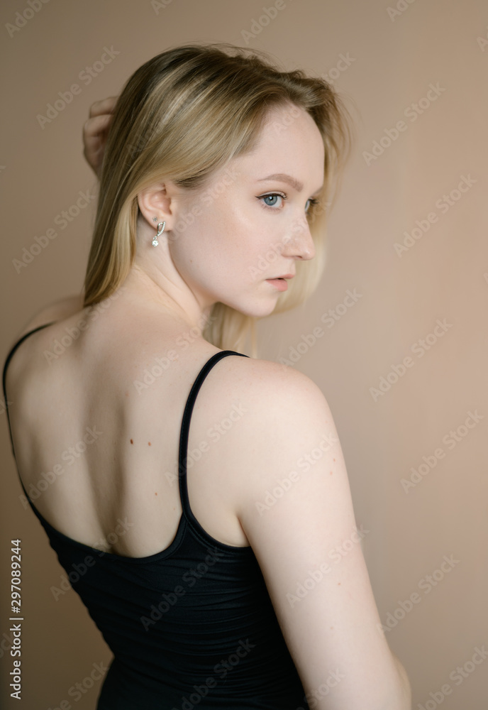 Graceful young woman in a black top posing against beige wall. Graceful young woman in a black top posing against beige wall.