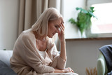 Sad mature woman sitting alone at home feeling headache depression