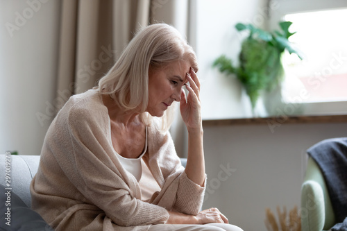 Sad mature woman sitting alone at home feeling headache depression photo
