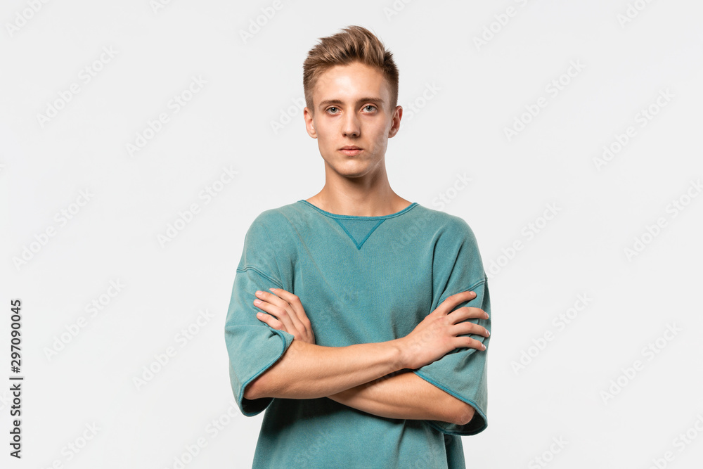 Confedent young man in a green tee holds hands folded isolated over grey background. Confedent young man in a green tee holds hands folded isolated over grey background.