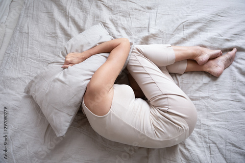Photo Frightened mature woman lying on bed fetal position covering pillow