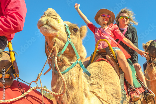 Happy camel riding couple in Australian desert of Northern Territory. Caucasian tourists enjoys camel ride on red dunes of Red Centre, Central Australia surrounds of Uluru and Kata Tjuta. photo