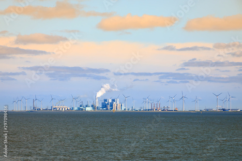 Factories and a coal-fired power plant surrounded by wind turbines