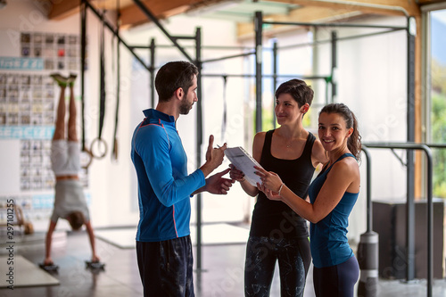 Gym instructor assisting two sporty women in fitness center.Concept of exercises