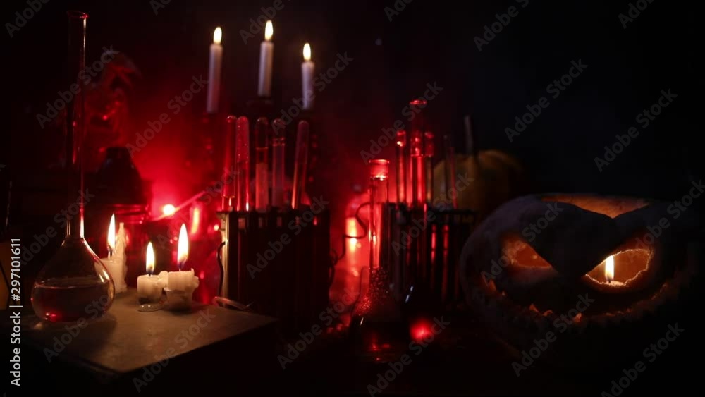 Wizard's Desk. Horror Halloween concept. Magic potions in bottles on wooden table with books and candles. Halloween still-life background with different elements on dark toned foggy background. Select Wizard's Desk. Horror Halloween concept. Magic potions in bottles on wooden table with books and candles. Halloween still-life background with different elements on dark toned foggy background. Select