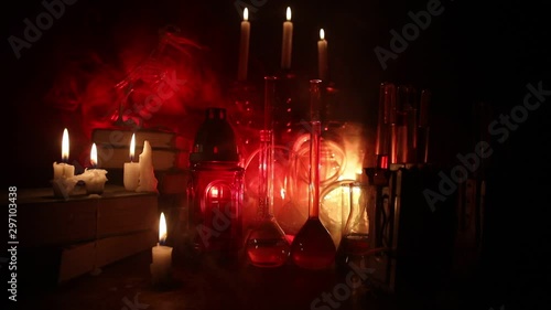 Wizard's Desk. Horror Halloween concept. Magic potions in bottles on wooden table with books and candles. Halloween still-life background with different elements on dark toned foggy background. Select