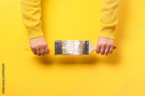 Paint brush in the hand of a girl on a yellow background, concept of apartment repair and painting works photo