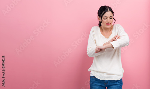 Young woman scratching her itchy arm. Skin problem. on a pink background