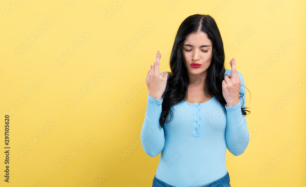 Young woman crossing her fingers and wishing for good luck on a yellow background Young woman crossing her fingers and wishing for good luck on a yellow background