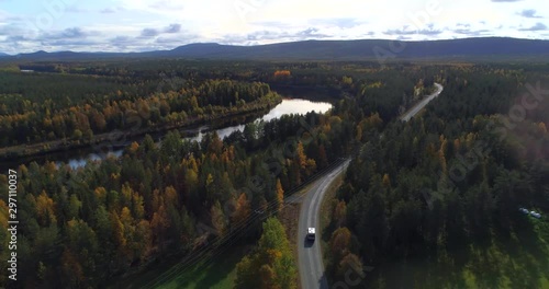 Caravan on a forest road, Aerial, drone shot, of a camper van, driving on a asphalt route, in middle of fall colored trees, on a partly sunny, autumn day, in Pyha-Luosto national park, Finland photo