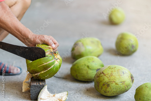 Green fresh coconut peeling and shelling with heavy chop knife for juice.