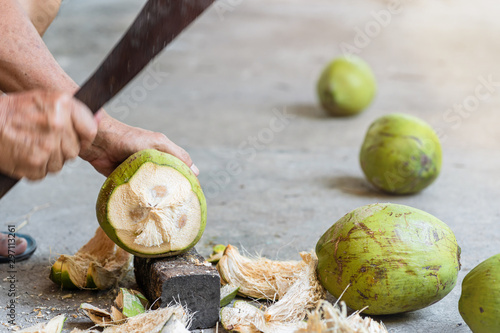 Green fresh coconut peeling and shelling with heavy chop knife for juice.
