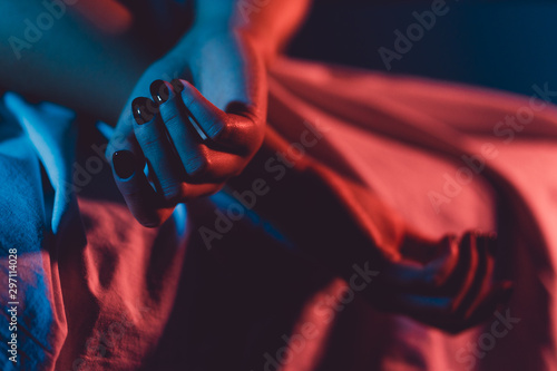 Close up on female young woman's girl's beautiful hands with black nail polish in dark room crossed fingers on the bed sheet gentle passion love temptation emotion love concept