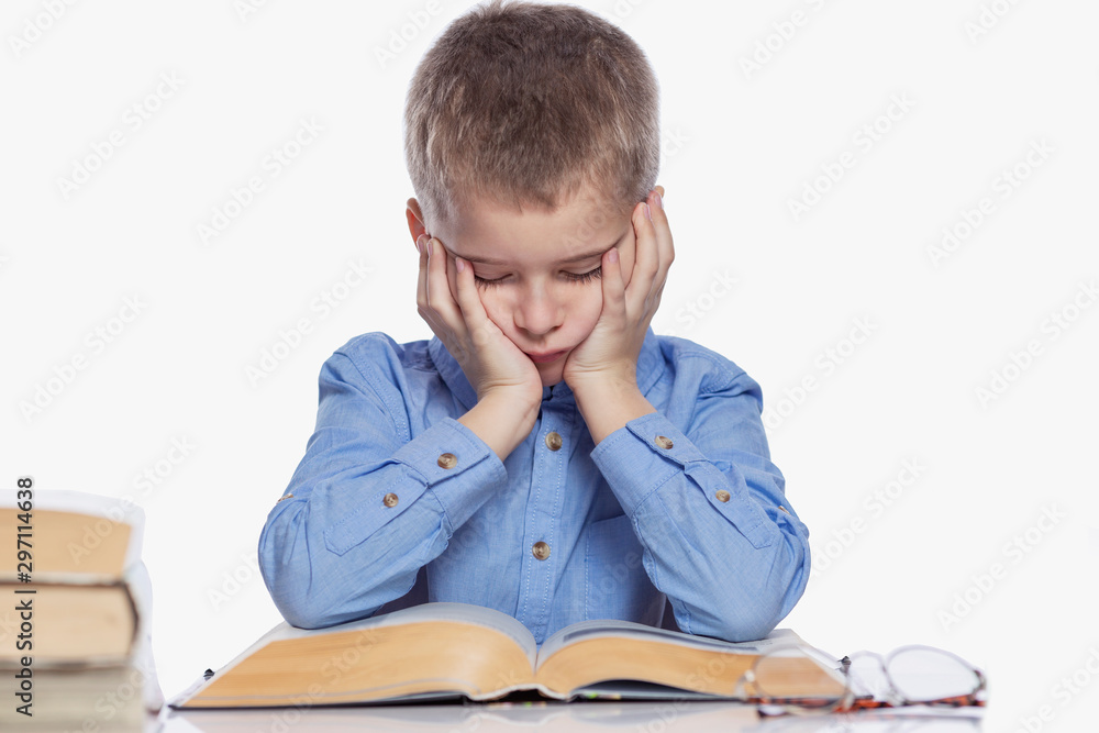 A schoolboy is doing homework at the table. Sadness and tiredness from studying. Isolated over white background. A schoolboy is doing homework at the table. Sadness and tiredness from studying. Isolated over white background.