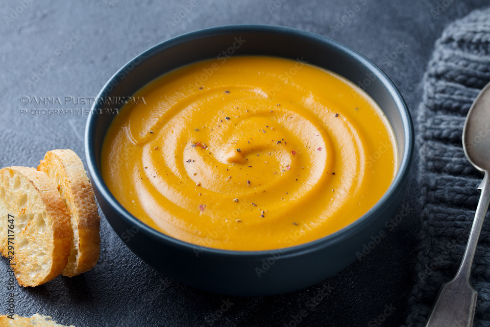 Pumpkin, carrot cream soup in a bowl. Grey background. Close up. Pumpkin, carrot cream soup in a bowl. Grey background. Close up.