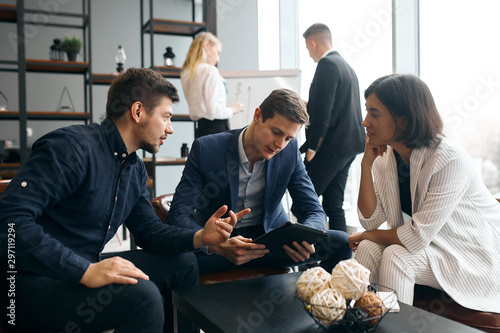 young business people discussing the positive and negative sides of problem, man holiding tabllet in hands, working with gadget photo