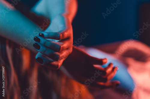 Close up on female young woman's girl's beautiful hands woman lying on the bed with black nail polish in dark room crossed fingers on sheet gentle passion love temptation emotion concept photo