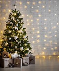 decorated christmas tree with white balls, garlands and gift boxes over white brick wall