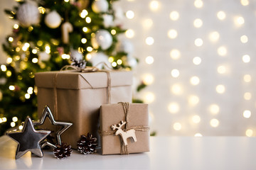christmas and new year background - gift boxes and stars near decorated christmas tree and copy space over white wall with lights