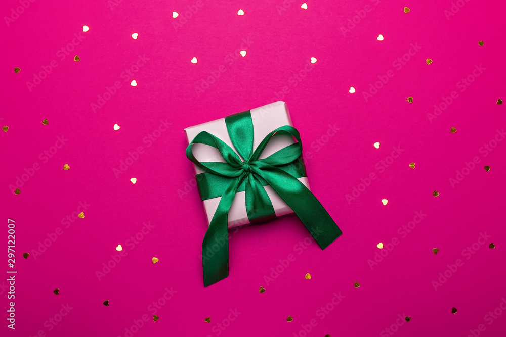 Wrapped present or giftbox with green ribbon on deep red or magenta background with hearts confetti, copy space, top view, flat lay. Background for Valentine's Day, Mother's Day or anniversary Wrapped present or giftbox with green ribbon on deep red or magenta background with hearts confetti, copy space, top view, flat lay. Background for Valentine's Day, Mother's Day or anniversary