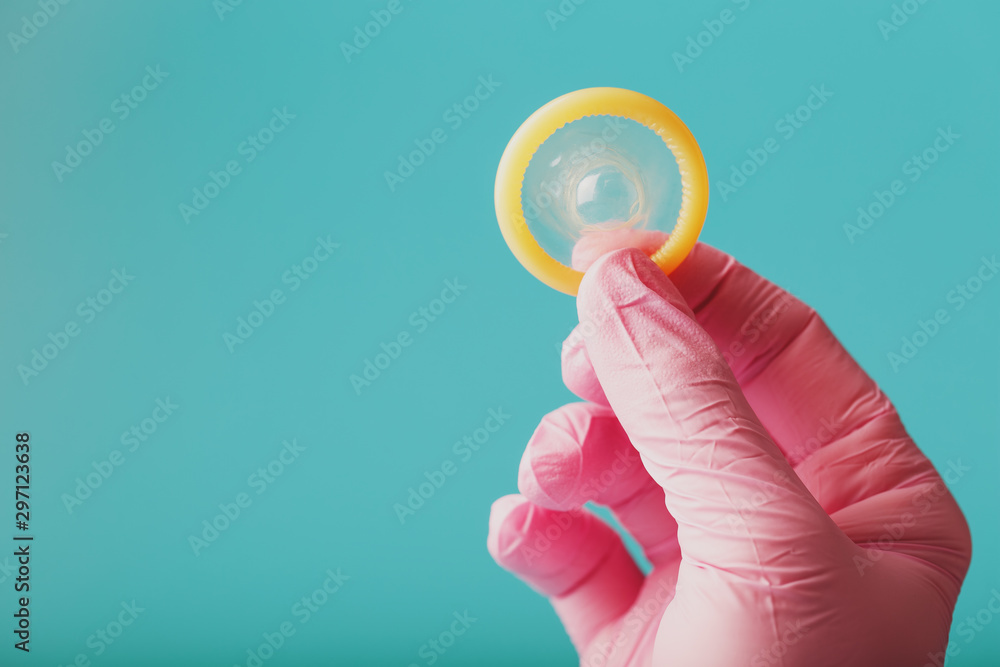 An opened condom in a hand in a pink glove holds on a blue background. Latex for protection