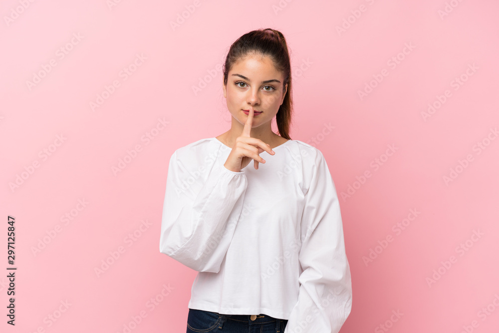 Young brunette girl over isolated pink background showing a sign of silence gesture putting finger in mouth Young brunette girl over isolated pink background showing a sign of silence gesture putting finger in mouth
