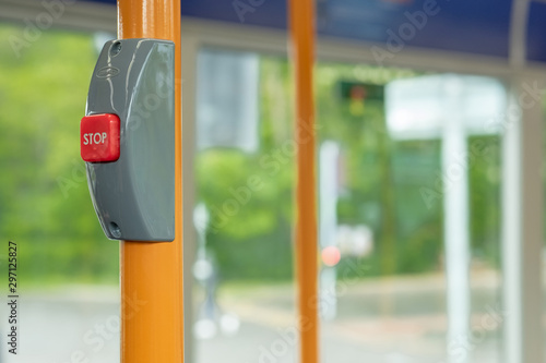Shallow focus of a red stop button seen inside a public bus. Used to request the driver to stop at a forthcoming bus stop. Seen with yellow handrails during a busy commute