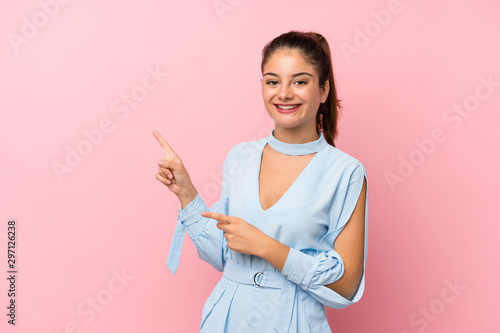 Young brunette girl over isolated pink background pointing finger to the side