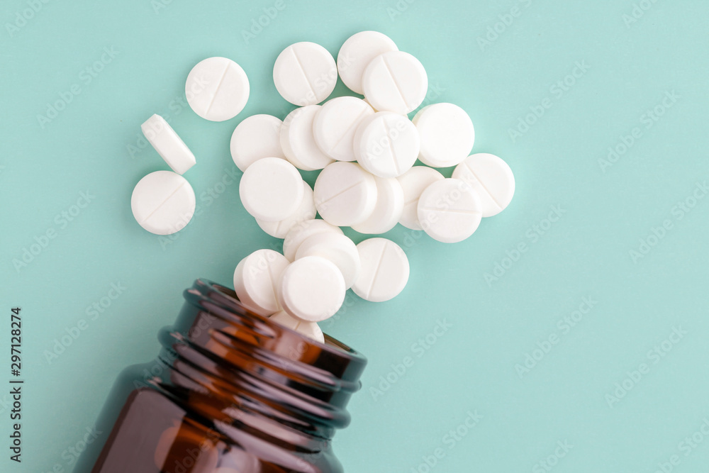 White round tablets scattered near glass bottle of pills White round tablets scattered near glass bottle of pills