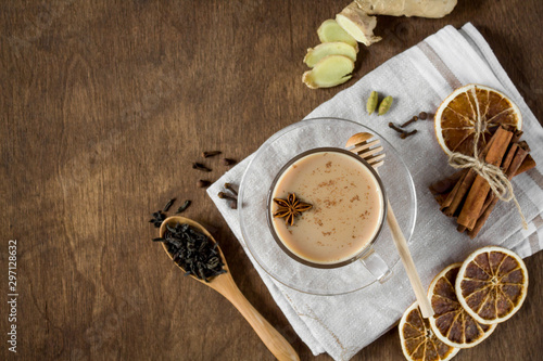 Masala chai tea and ingredients on wooden background. Traditional Indian hot drink made of milk and tea with spices. Copy space, top view.