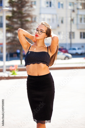 Sexy beautiful young brunette woman in skirt and black bra, posing on summer street