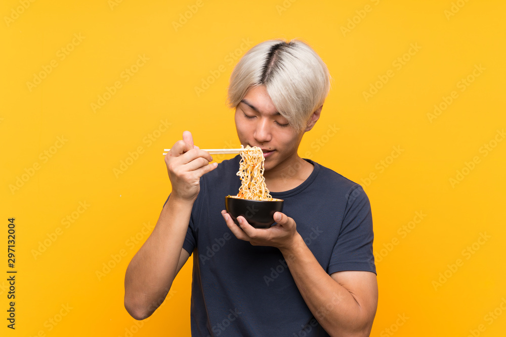 Young asian man with noodles over isolated yellow background Young asian man with noodles over isolated yellow background