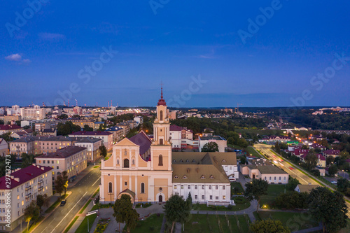 Holy Cross Church And Traffic In Mostowaja And Kirova Streets At Evening In Night Illuminations Lights. Sunset Sky. Grodno city in Belarus