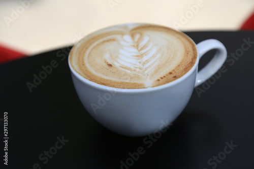 Cup of cappuccino with latte art. Hot coffee on table. White cup of cappuccino stands on the table, selective focus © Ihor
